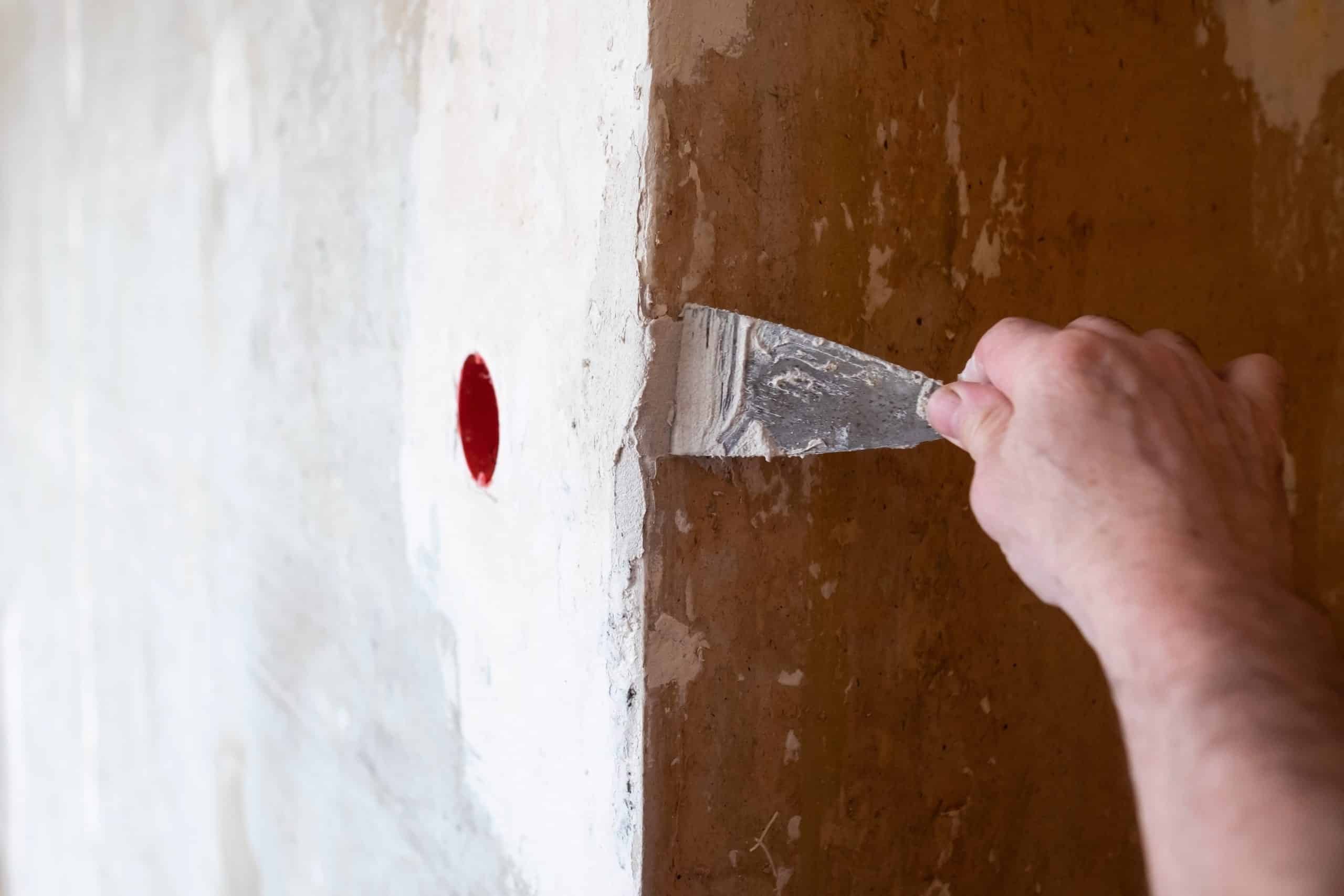 Close-up of a putty knife pressing spackle into a small nail hole in a painted wall