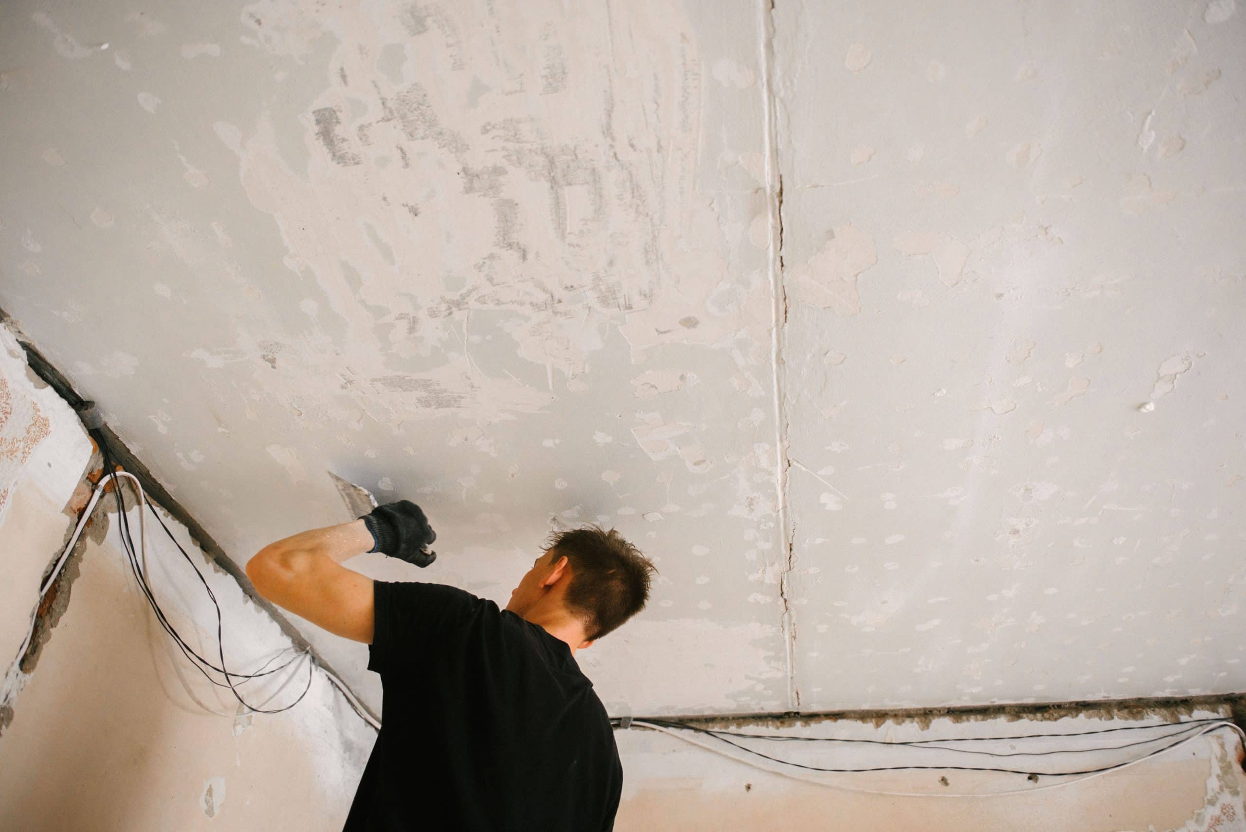 Close-up of a spatula scraping old paint and texture off a ceiling down to the bare surface