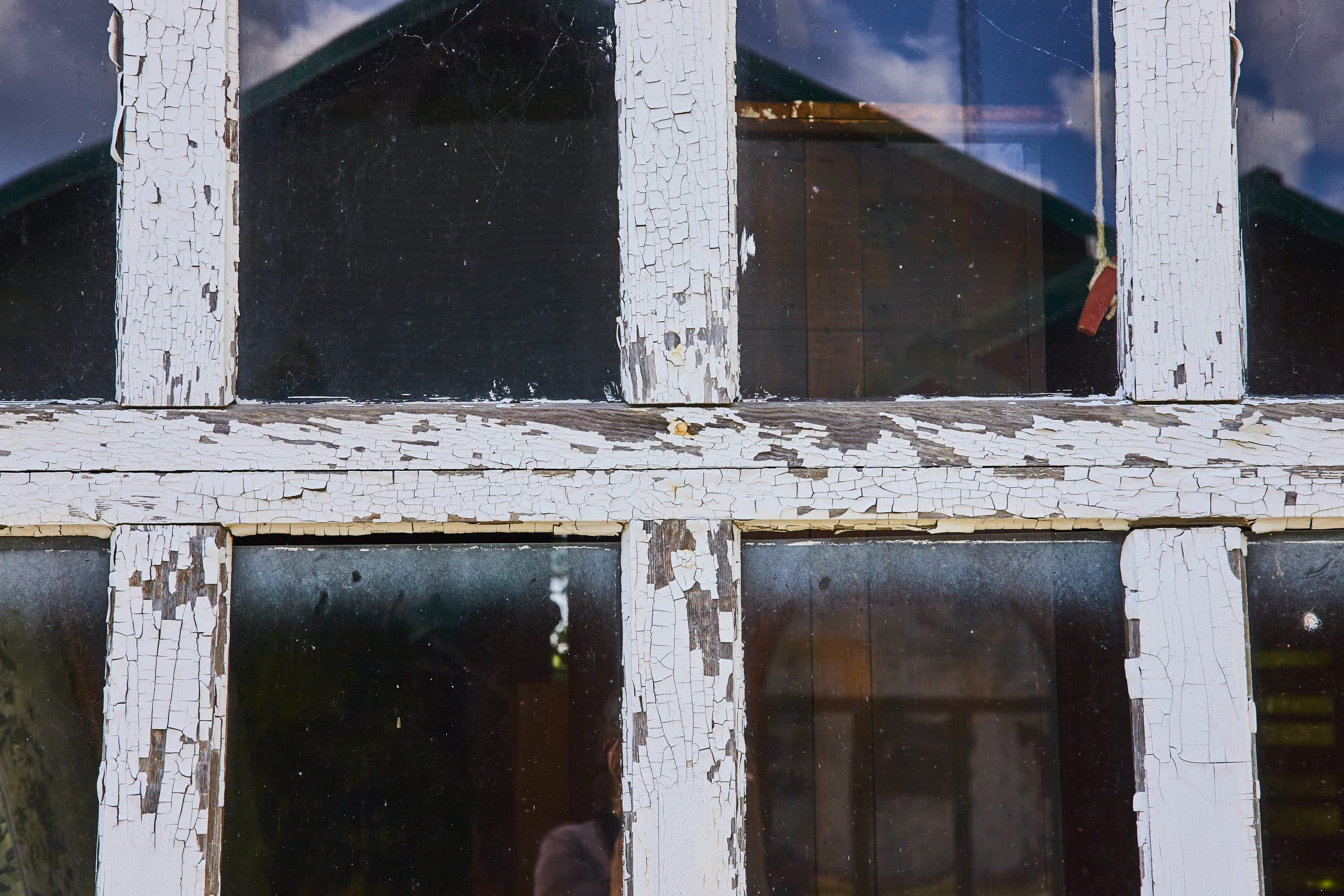 Weathered window frame with paint peeling and bubbling near the sill, the kind of damage repeated condensation leaves behind over a few winters