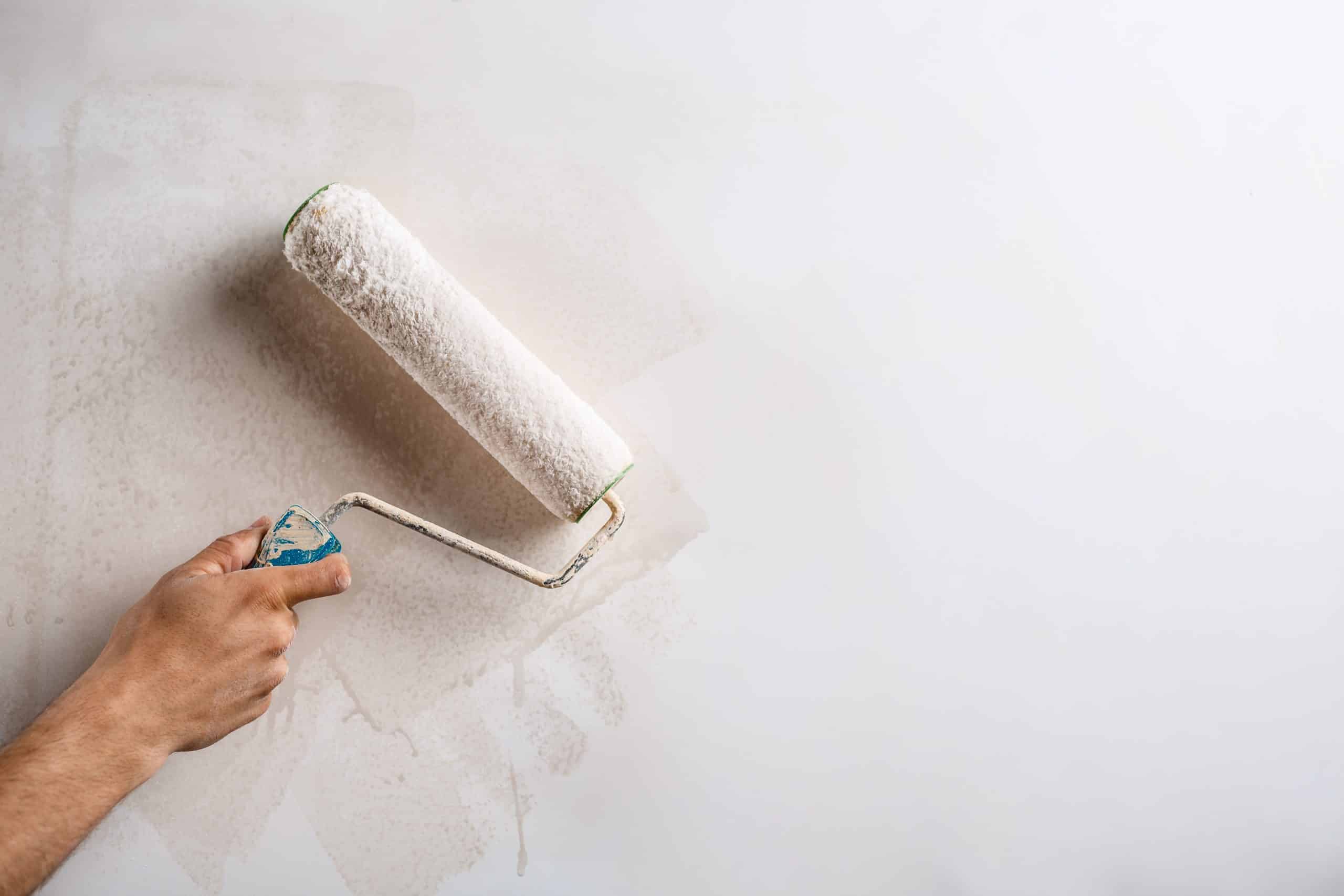 Close-up of a hand rolling primer onto an interior wall after scraping off peeling paint