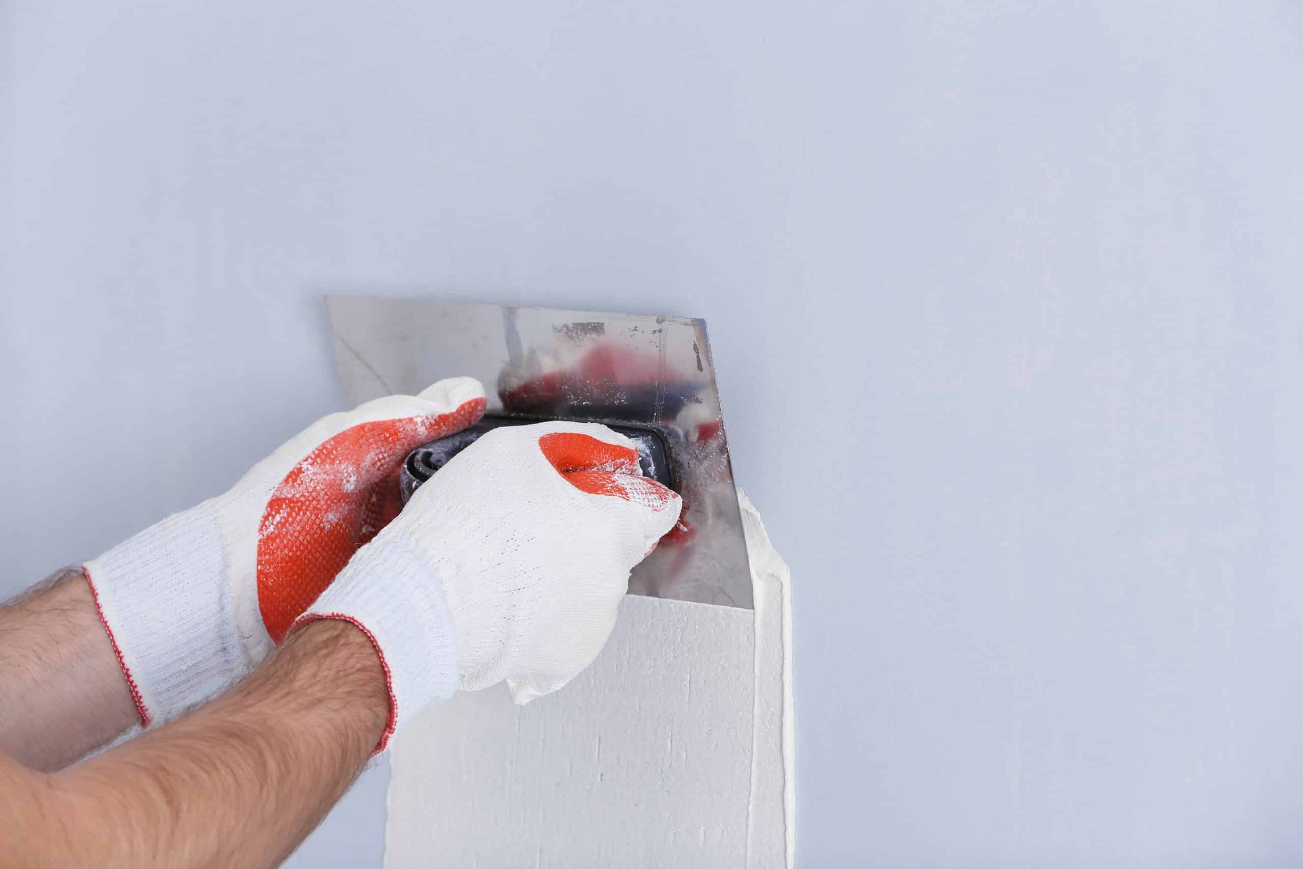 Worker feathering joint compound several inches past the edge of a filled drywall dent with a wide taping knife