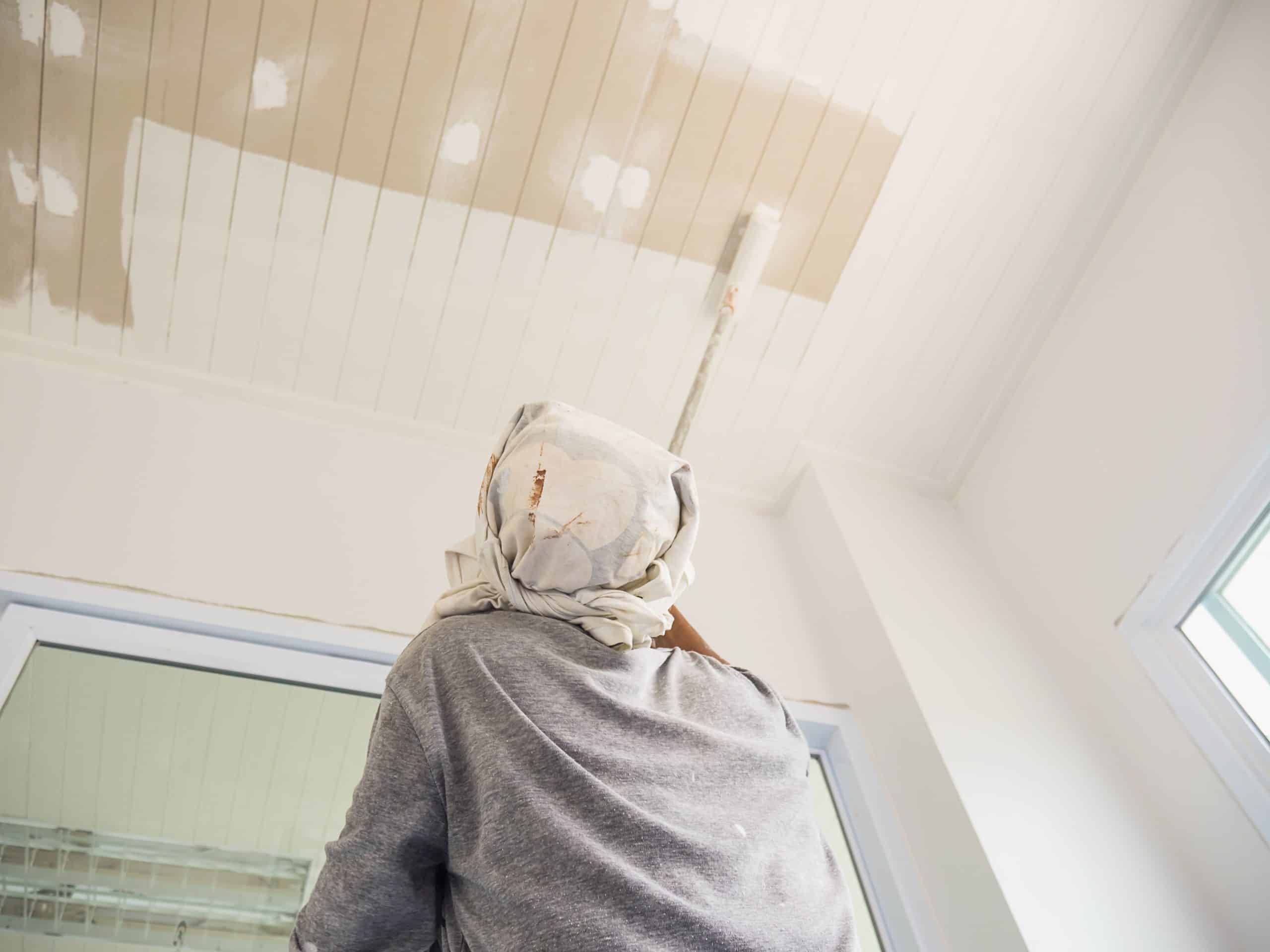 Painting a ceiling with a roller after sealing a water stain with stain-blocking primer