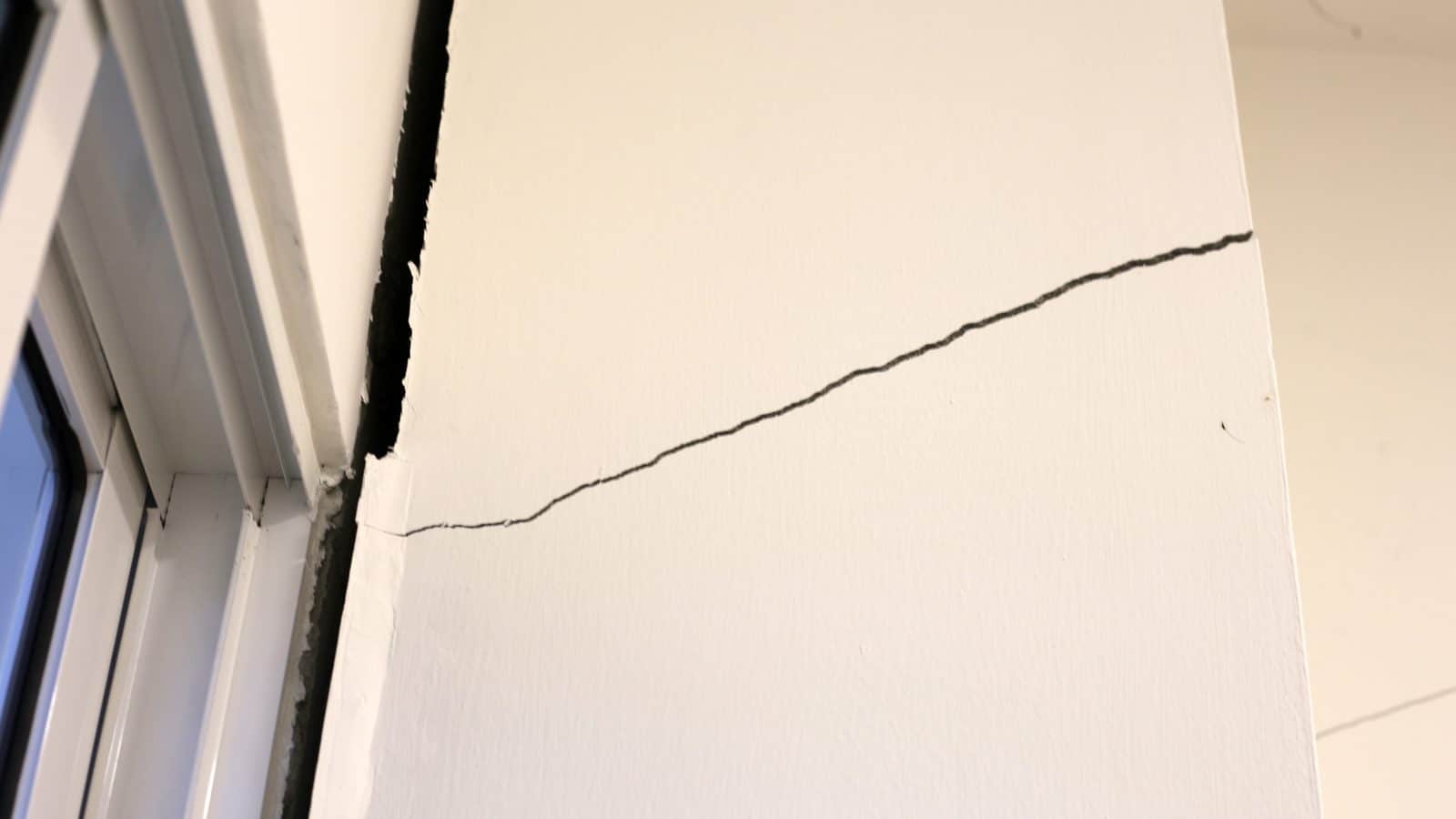 Diagonal crack running across a white interior wall from the top corner of a window frame