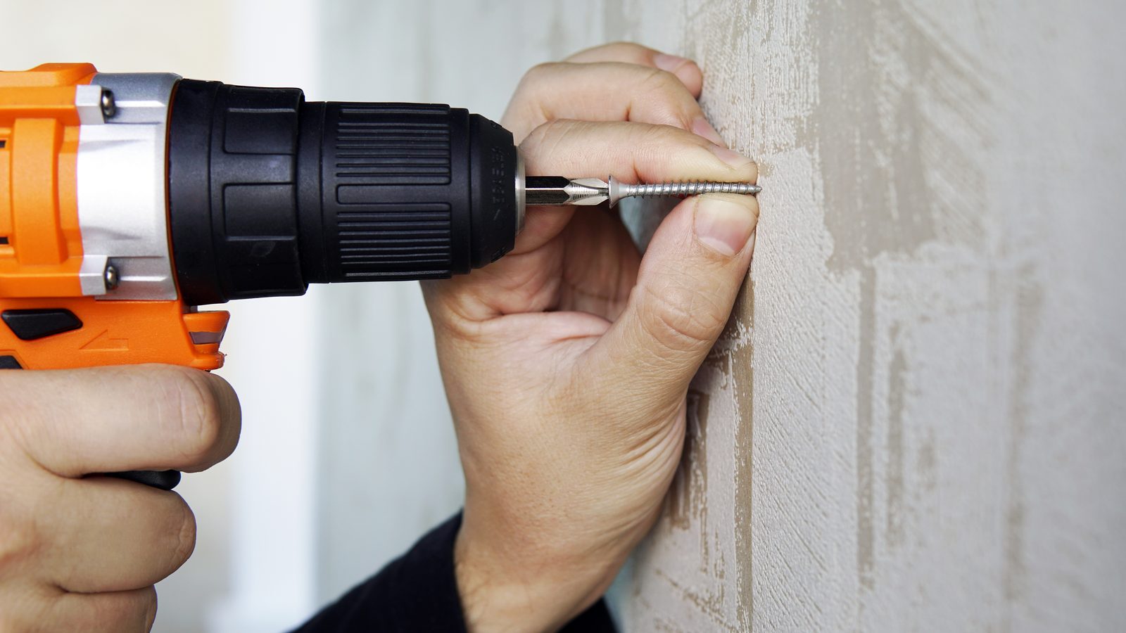 Drill driving a drywall screw an inch beside a popped nail head so the board is pulled tight to the stud