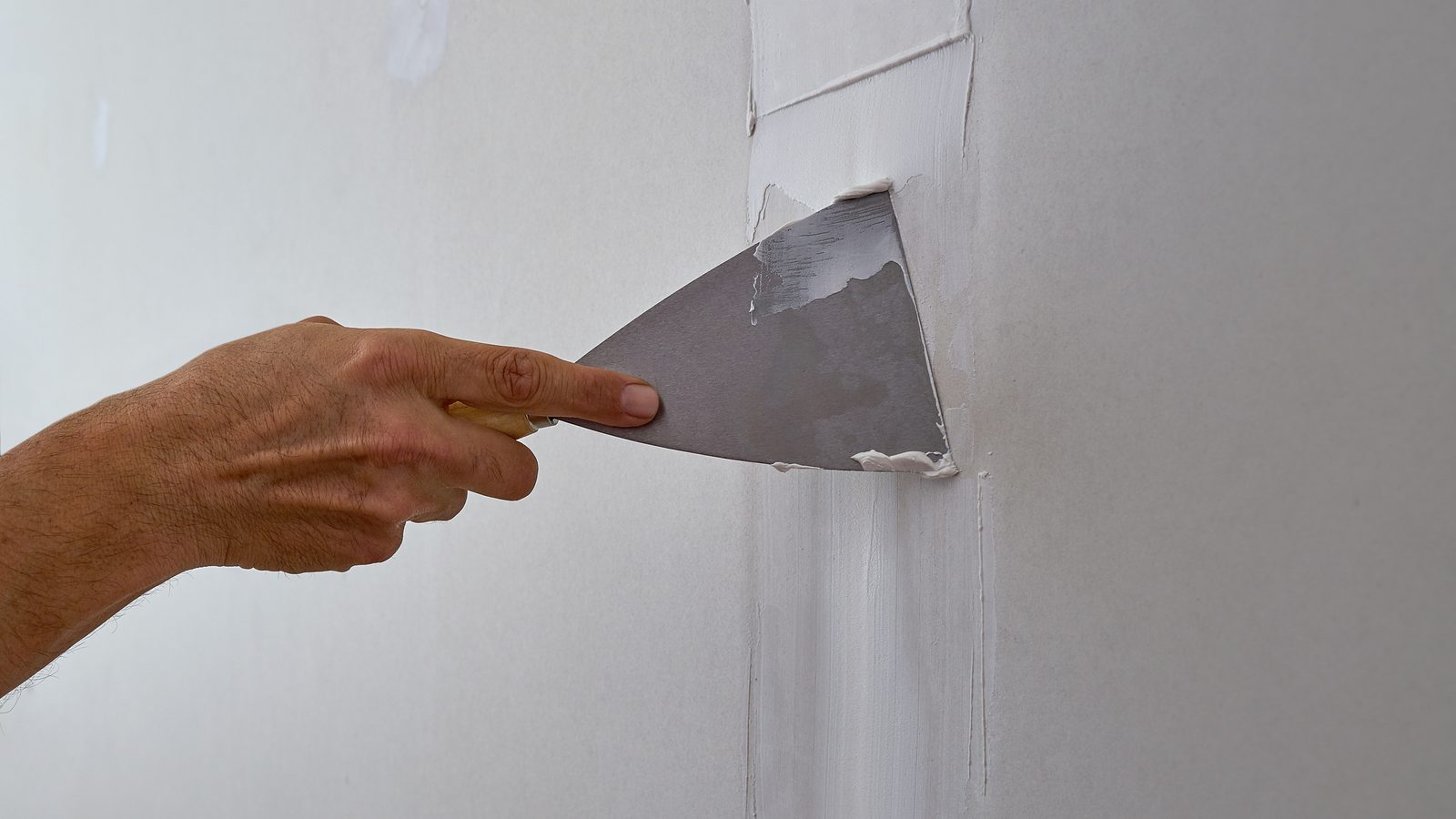 Hand running a taping knife along a drywall seam to lay a second coat of compound over the taped joint