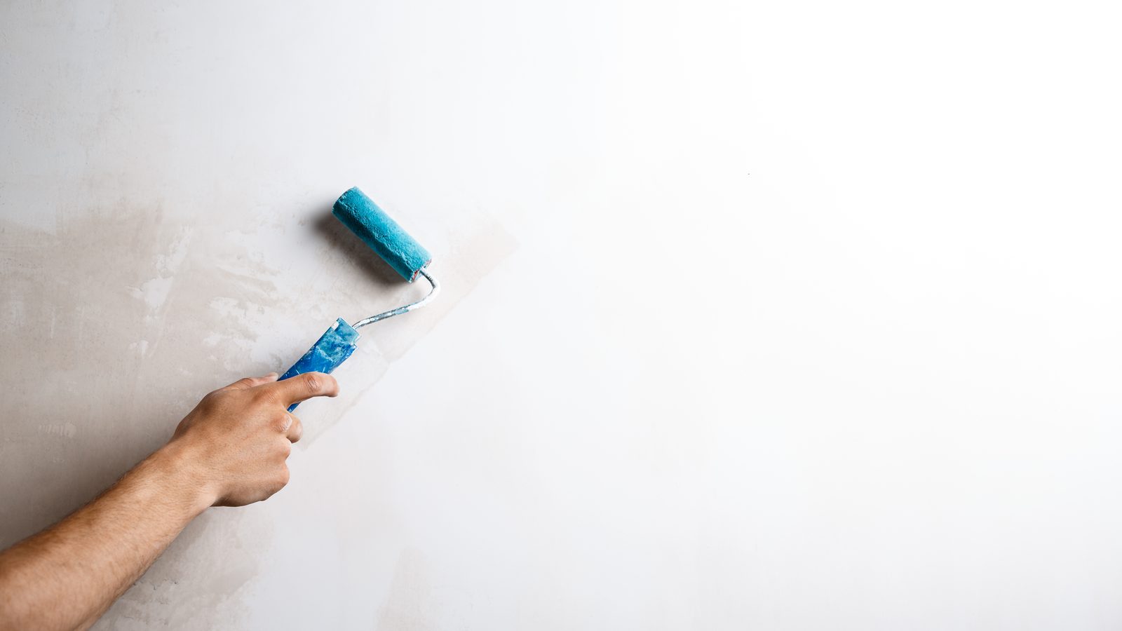 Hand rolling a small patch of fresh paint onto a white wall with a blue mini roller
