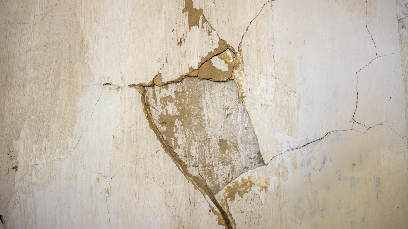 Shallow crater in an old plaster wall with fine cracks radiating outward and loose plaster chipped away around it