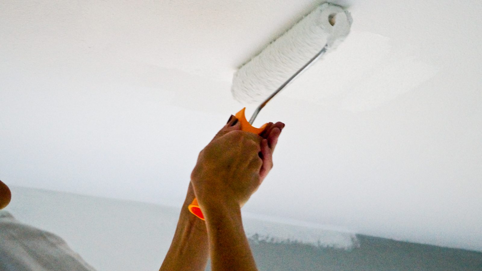 Hand rolling a fresh stripe of white primer onto a ceiling with a short-nap roller