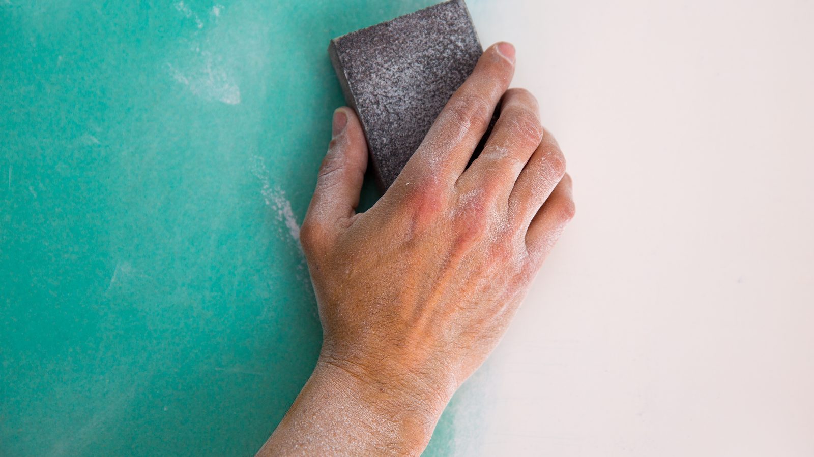 Hand working a sanding sponge over the dried joint compound on a taped drywall seam