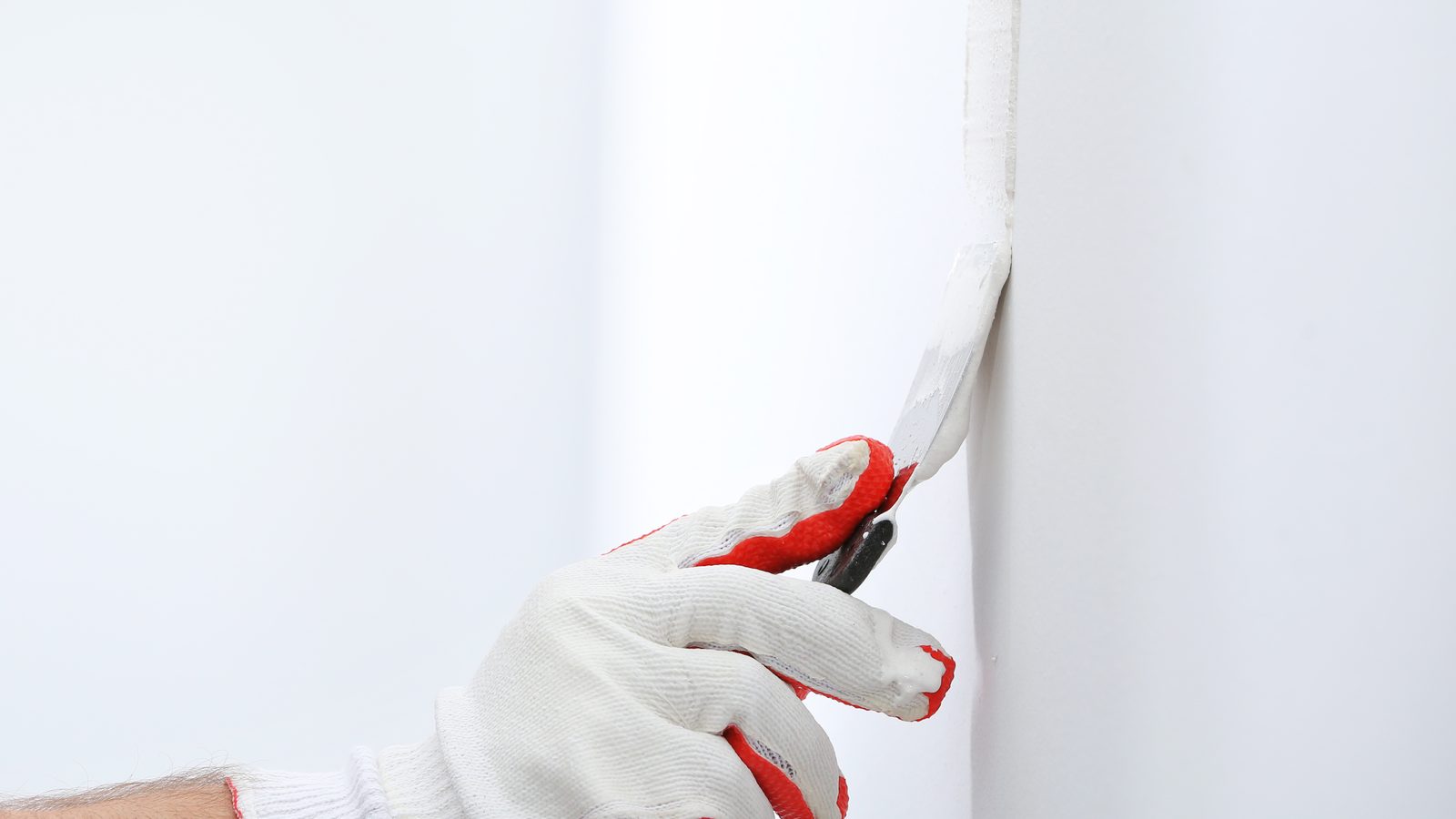 Gloved hand working a putty knife along a wallpaper edge at an inside corner to press it back down